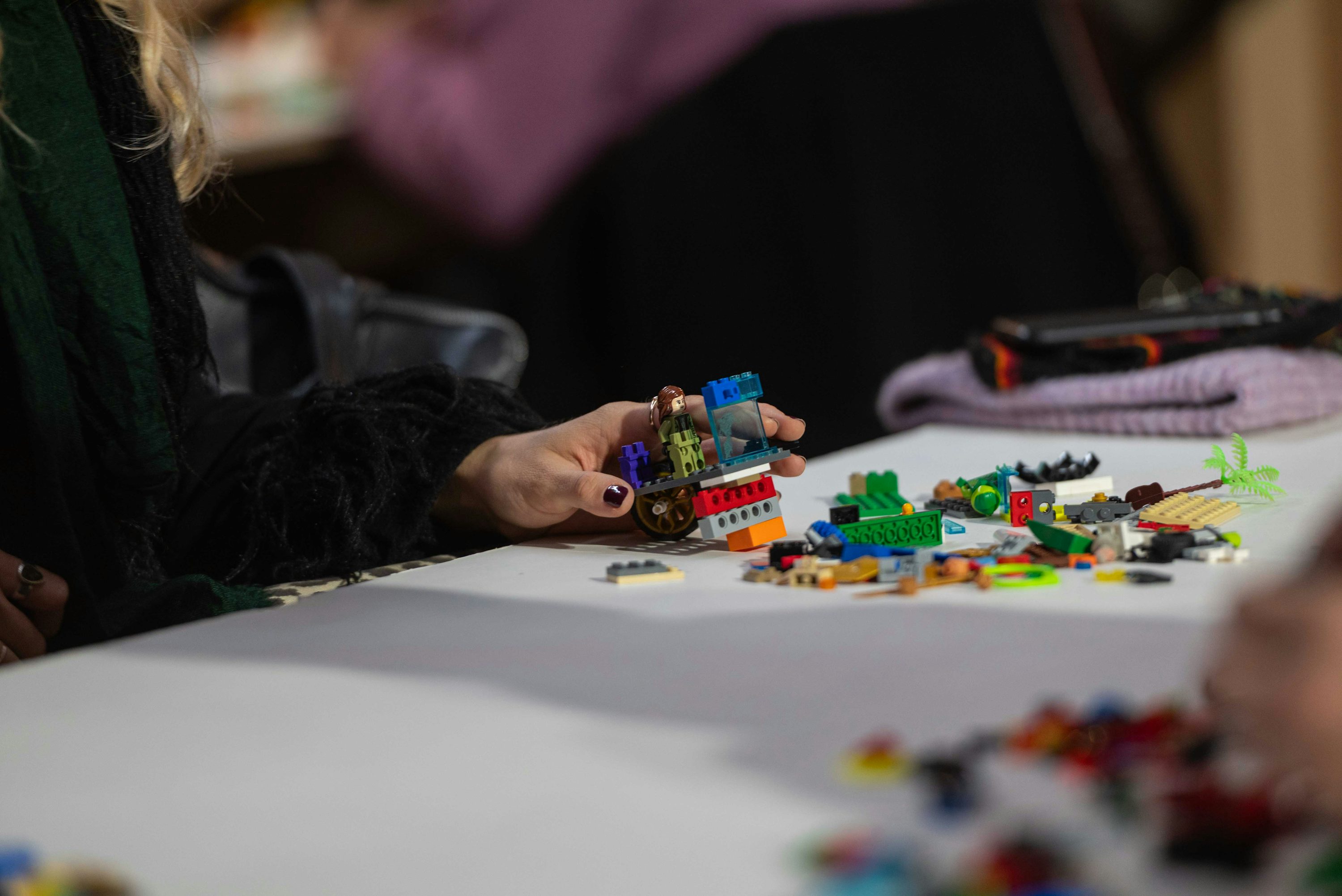 Hands assembling a colorful LEGO model at a table
